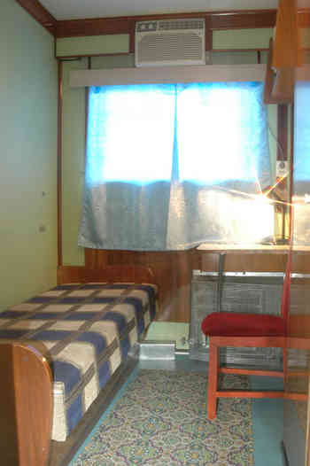 Одноместная каюта с умывальником на средней палубе. В каюте: односпальная кровать, столик, стул, шкаф для одежды, графин для воды, стаканы, светильник, кондиционер, встроенные полочки для книг, радиот